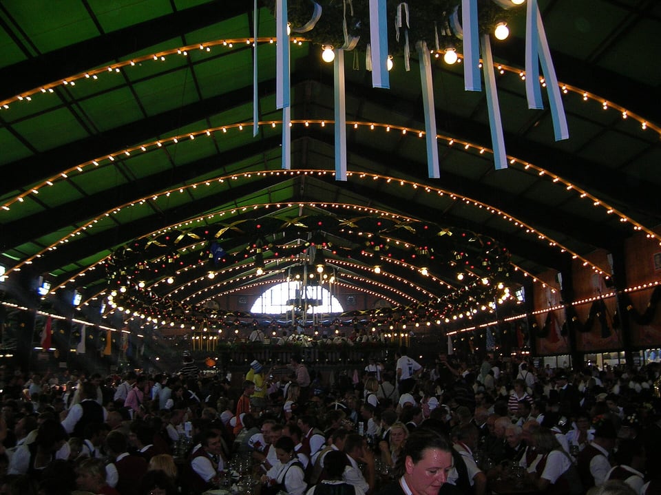 Visitors in traditional Bavarian clothing seated at long tables inside the decorated Augustiner Oktoberfest tent.