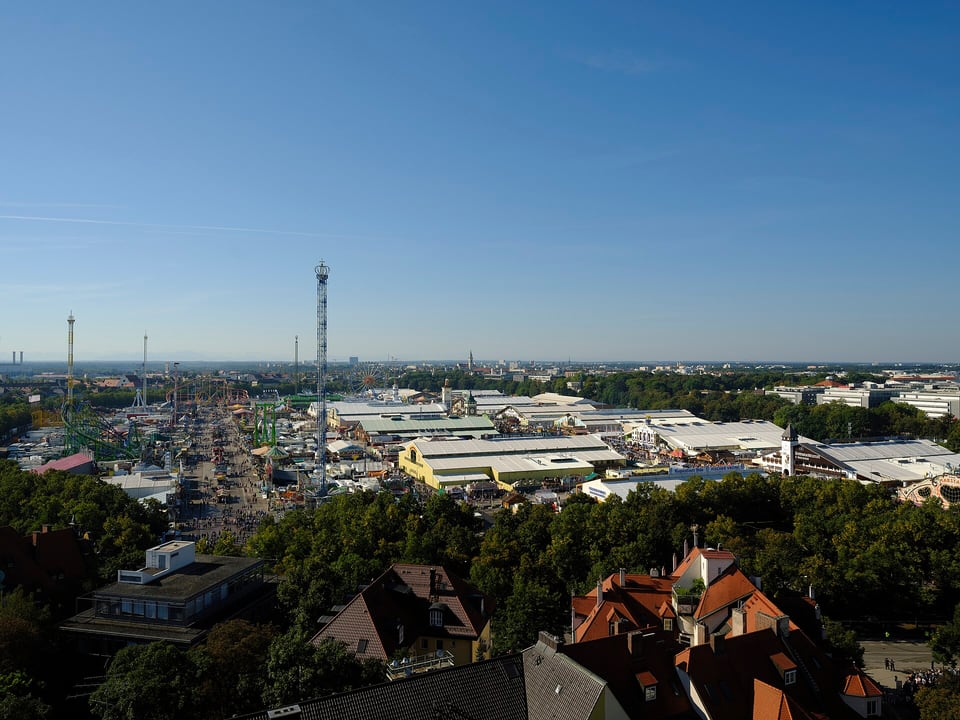 A wide view across the busy Oktoberfest grounds, festival tents, rides, and Ferris wheel on the Theresienwiese.